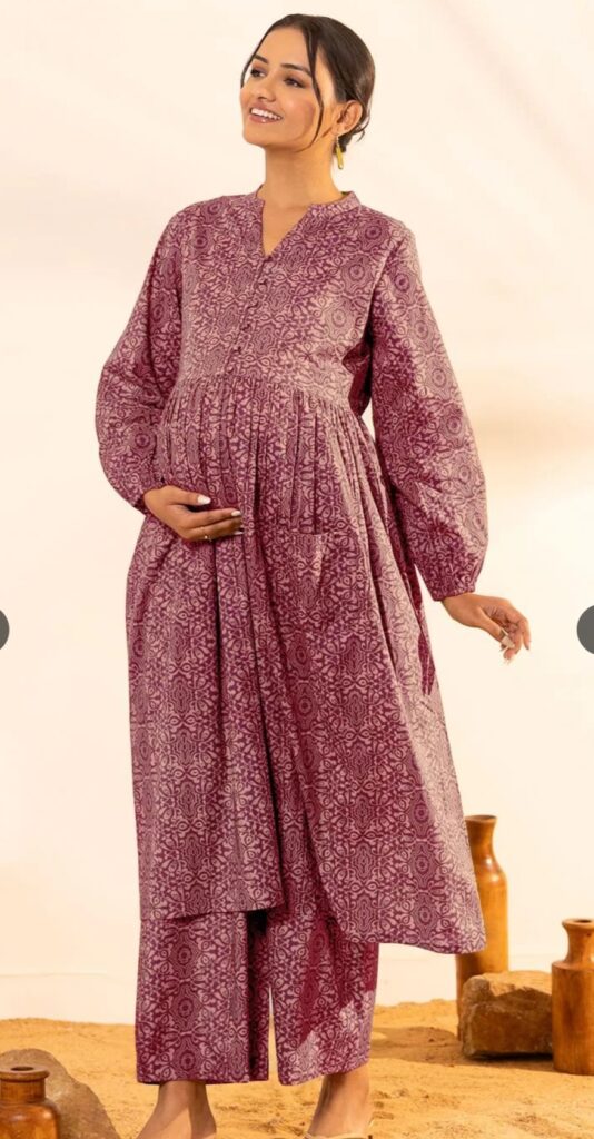 A smiling pregnant woman wears a maroon printed maternity kurta with matching trousers, featuring long sleeves and a comfortable, relaxed fit.