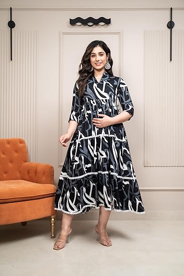 A Pregnant woman poses indoors wearing a stylish black and white printed flared maternity anarkali gown dress, paired with nude heels and statement earrings.