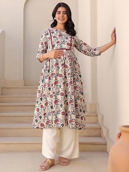 pregnant woman wearing floral printed A-line kurta with white palazzo pants, standing on stairs, posing against cream wall