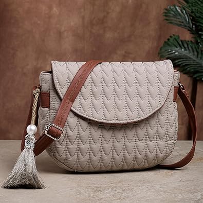 Stylish beige quilted sling bag with brown strap, flap closure, and decorative tassel, placed on table against rustic background.